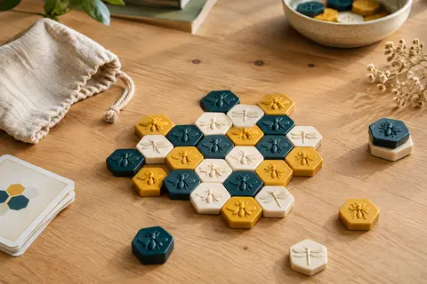 Pions hexagonaux de Hive disposés en ruche sur une table en bois clair, avec le sac de rangement à côté.